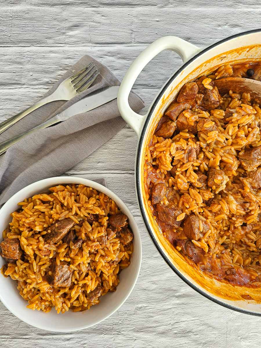 Greek lamb and tomato stew in a white bowl and pot, ready to serve