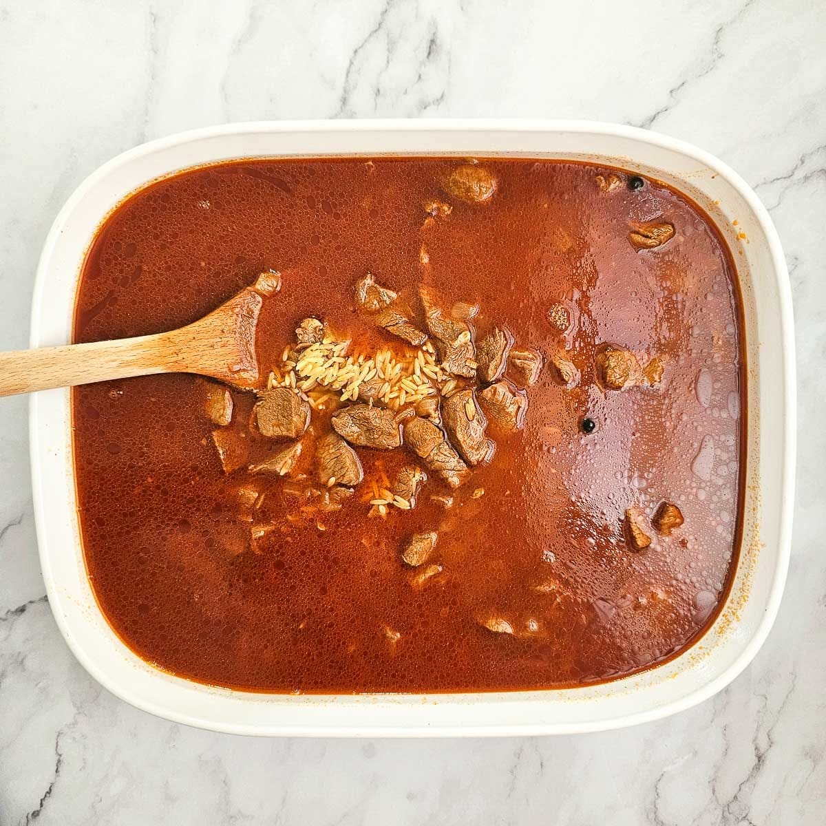 Greek lamb and tomato stew in baking dish adding orzo pasta