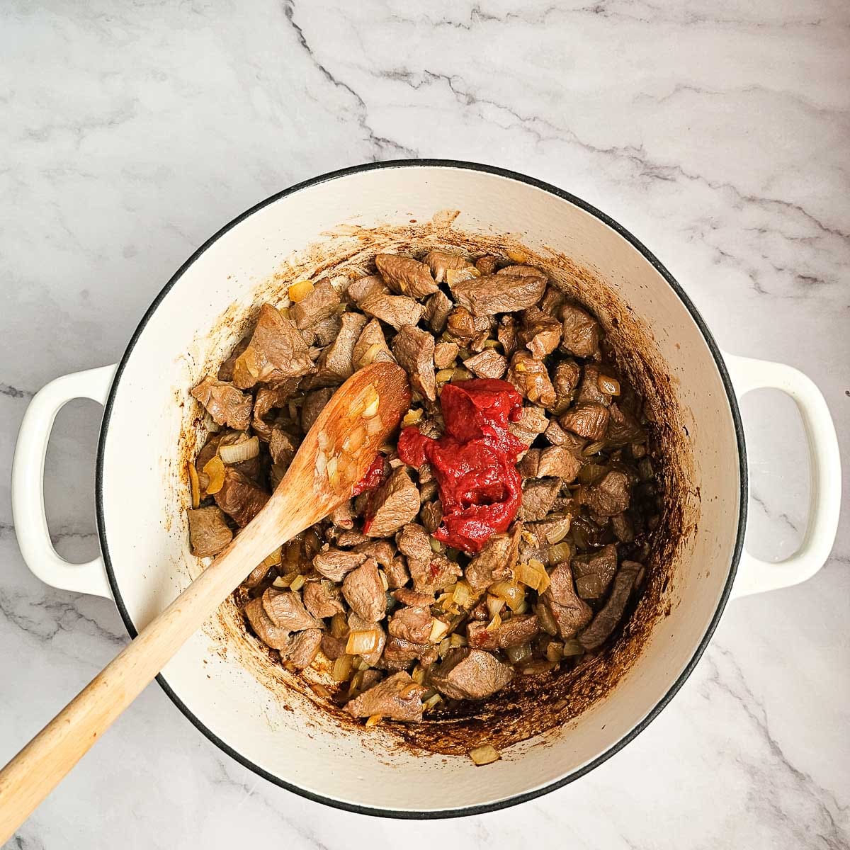 Greek lamb and tomato stew sauteing diced lamb in pot and adding tomato paste