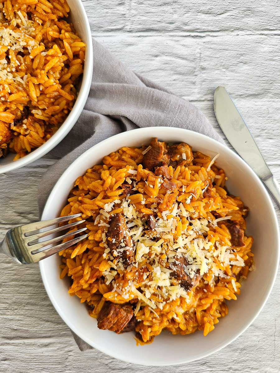 Greek lamb and tomato stew in white bowl with grated cheese ready to serve