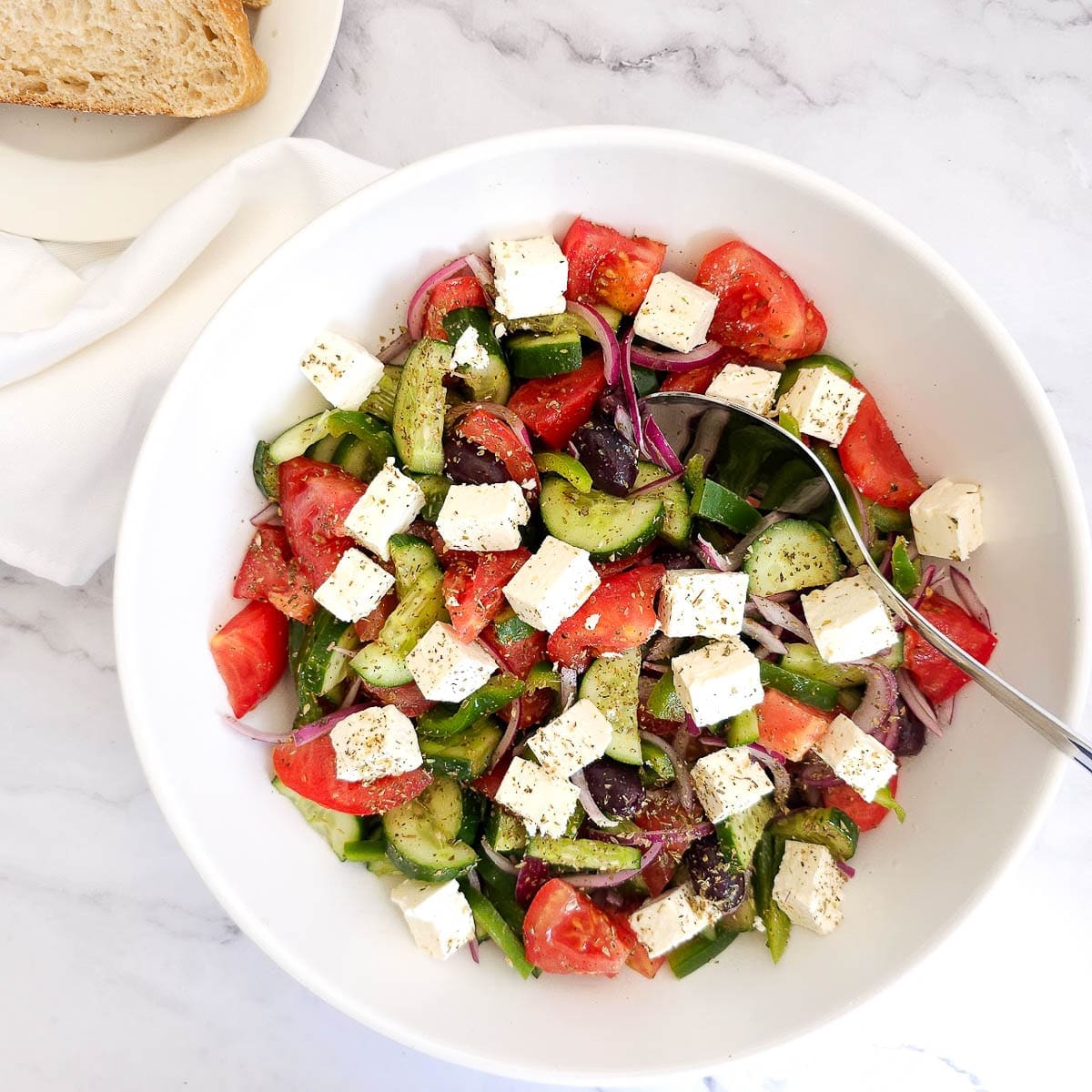 Greek salad in a white bowl with white napkin and bread