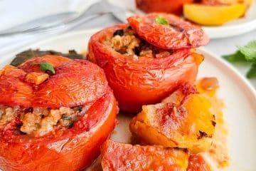 Greek stuffed tomatoes with rice- Yemista, on a white plate with some baked potatoes.