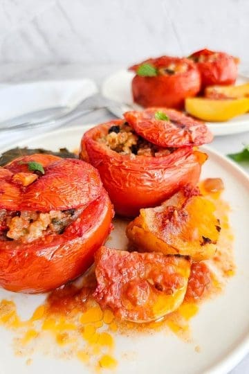 Greek stuffed tomatoes with rice- Yemista, on a white plate with some baked potatoes.