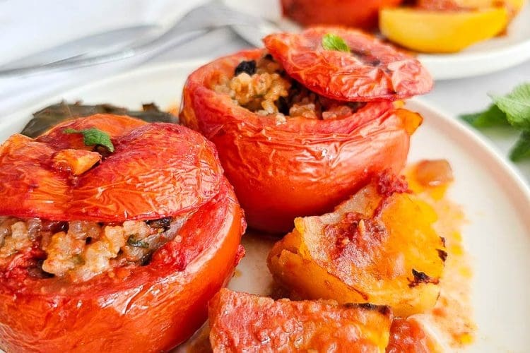 Greek stuffed tomatoes with rice- Yemista, on a white plate with some baked potatoes.