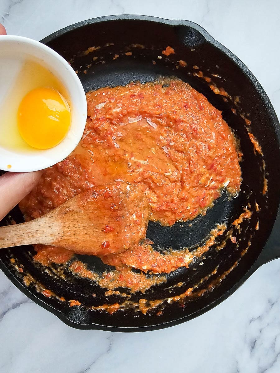 Adding eggs to a pan for Strapadsada-Greek scrambled eggs and tomatoes.