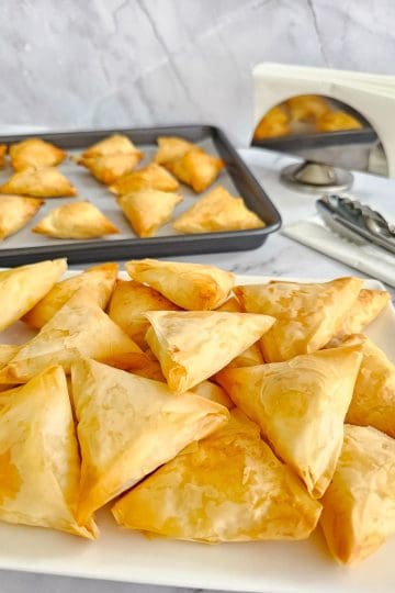 Greek cheese triangles-tiropitakia on a plate ready to serve and baking tray in background