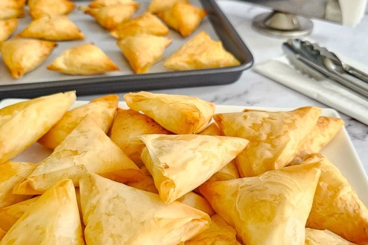 Greek cheese triangles-tiropitakia on a plate ready to serve and baking tray in background