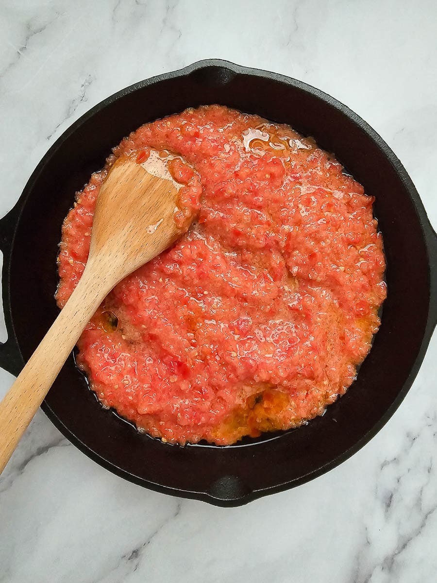 Frying crushed tomatoes in a pan for Strapadsada-Greek scrambled eggs and tomatoes.