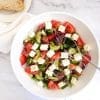 Greek salad with tomatoes, cucumber, feta, olives in a white bowl.