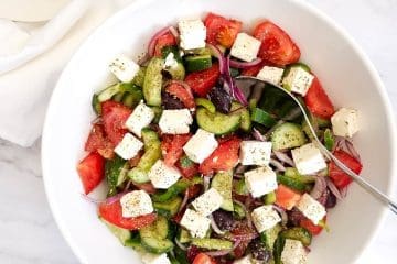 Greek salad with tomatoes, cucumber, feta, olives in a white bowl.