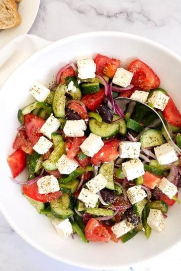 Greek salad with tomatoes, cucumber, feta, olives in a white bowl.