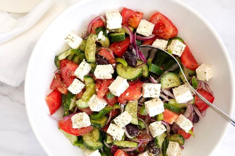 Greek salad with tomatoes, cucumber, feta, olives in a white bowl.