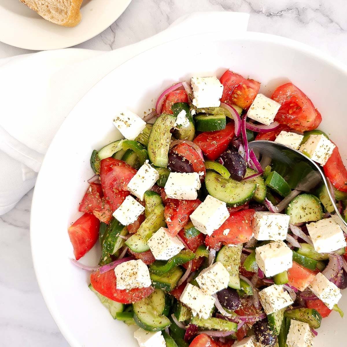 Greek salad with sliced tomatoes, cucumbers, feta cheese, olives, onions, and peppers in a white bowl