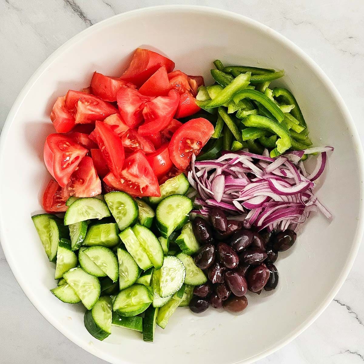 Greek salad-sliced tomatoes, cucumbers, onions, olives and peppers in a bowl