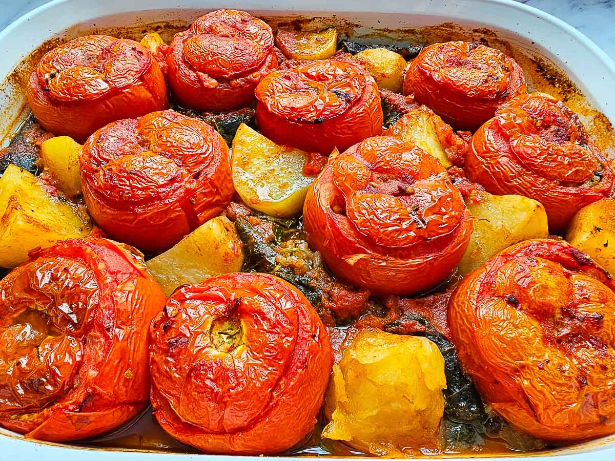 Baked Yemista, stuffed tomatoes with rice, in baking dish with potatoes and vine leaves.