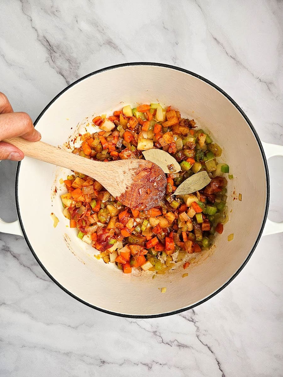 Greek lentil soup-fakes-saute onions, vegetables, tomato and bay leaves in pot. 