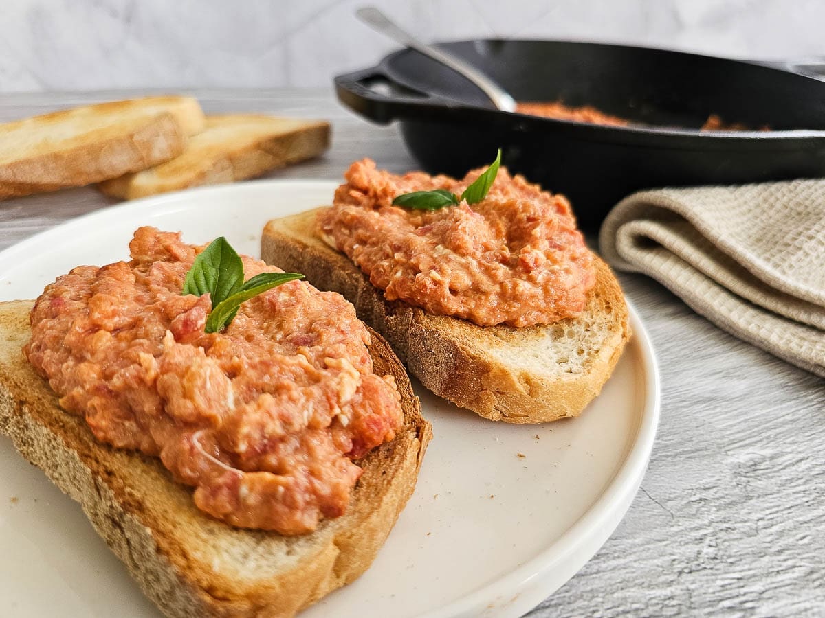 Strapatsada-Greek scrambled eggs and tomatoes in a pan and on a plate with sliced bread.