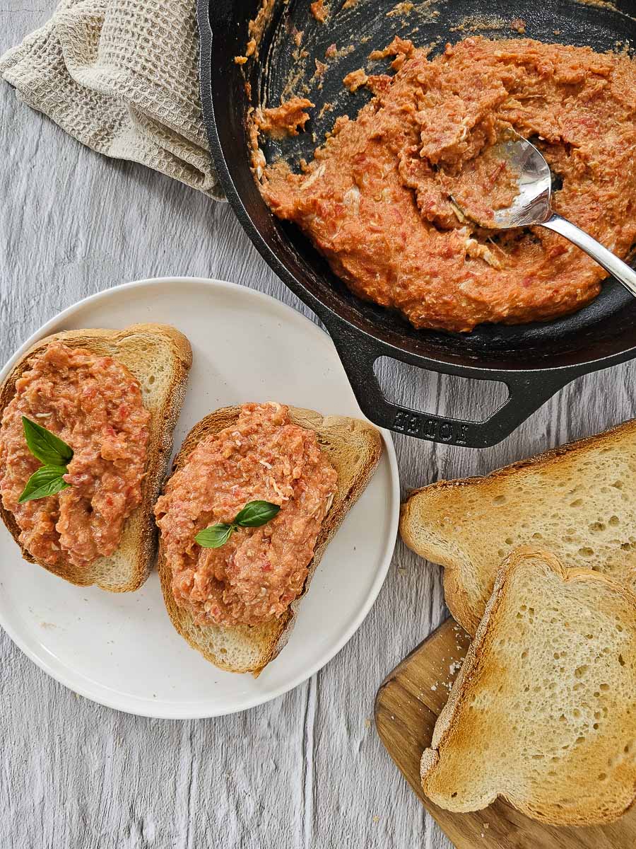 Strapadsada-Greek scrambled eggs and tomatoes in a pan and on a plate with sliced bread.