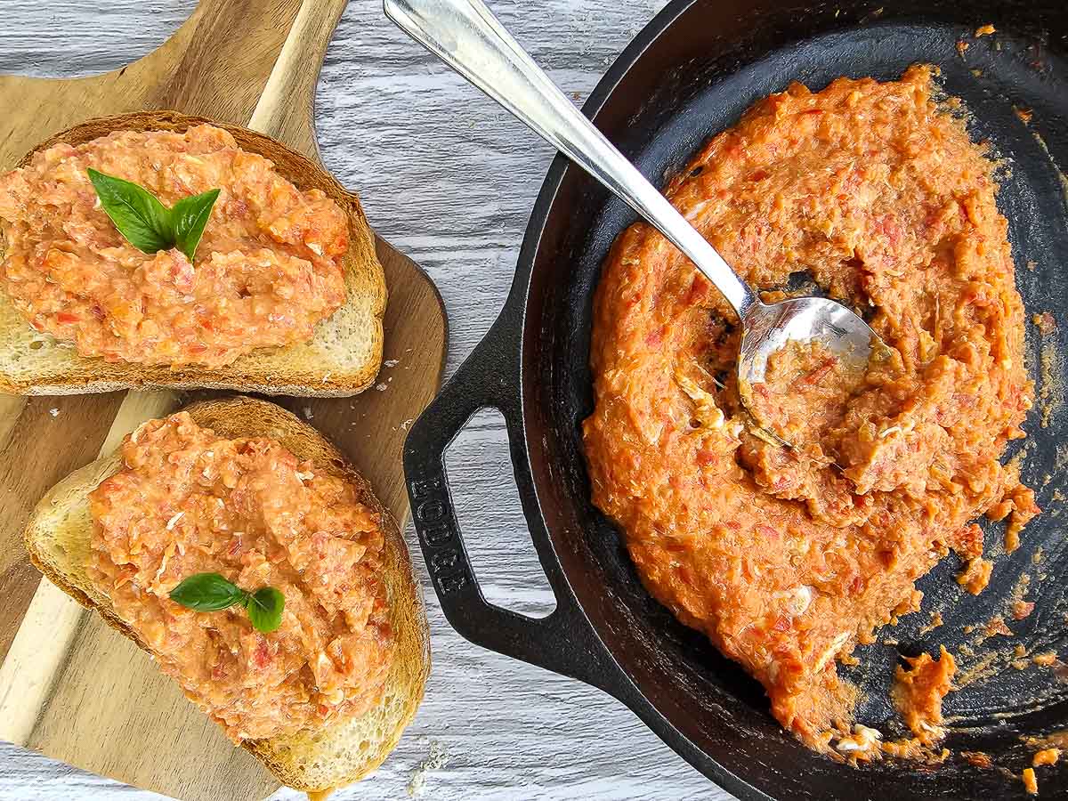 Strapatsada-Greek scrambled eggs and tomatoes in a pan with sliced bread on board.