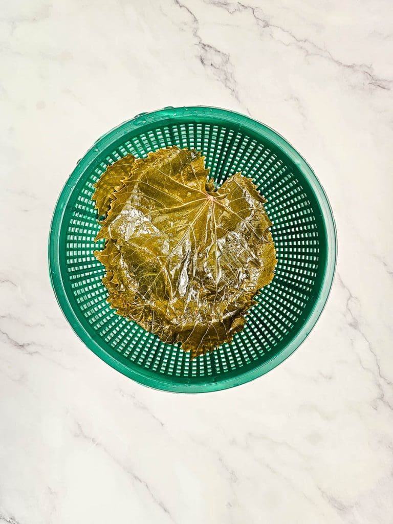 strained blanched vine leaves in colander.