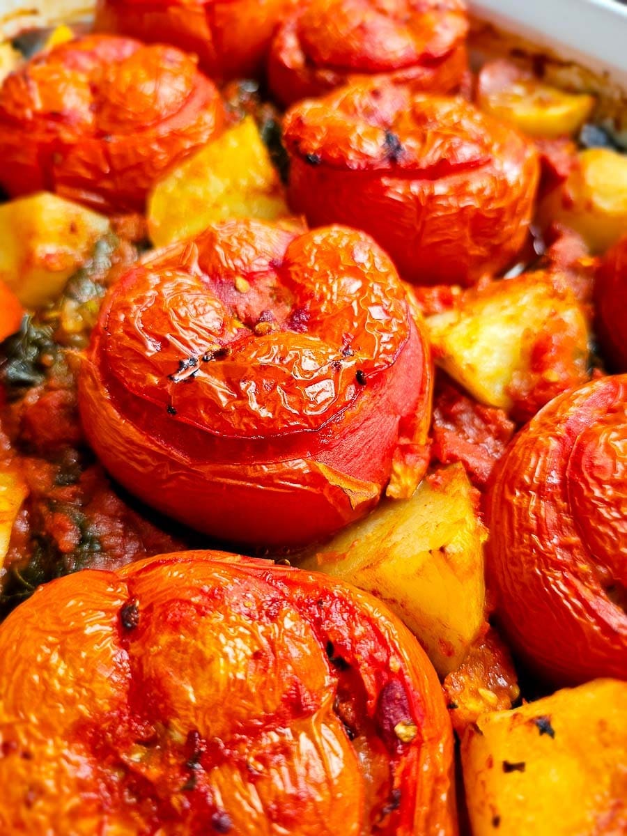 Baked Yemista, stuffed tomatoes with rice, in baking dish with potatoes and vine leaves.