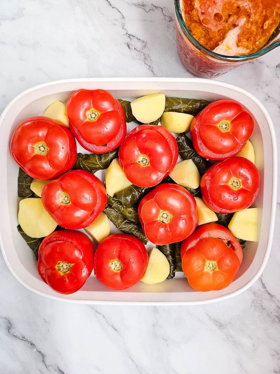 Yemista, stuffed tomatoes with rice, in baking dish with potatoes and vine leaves.