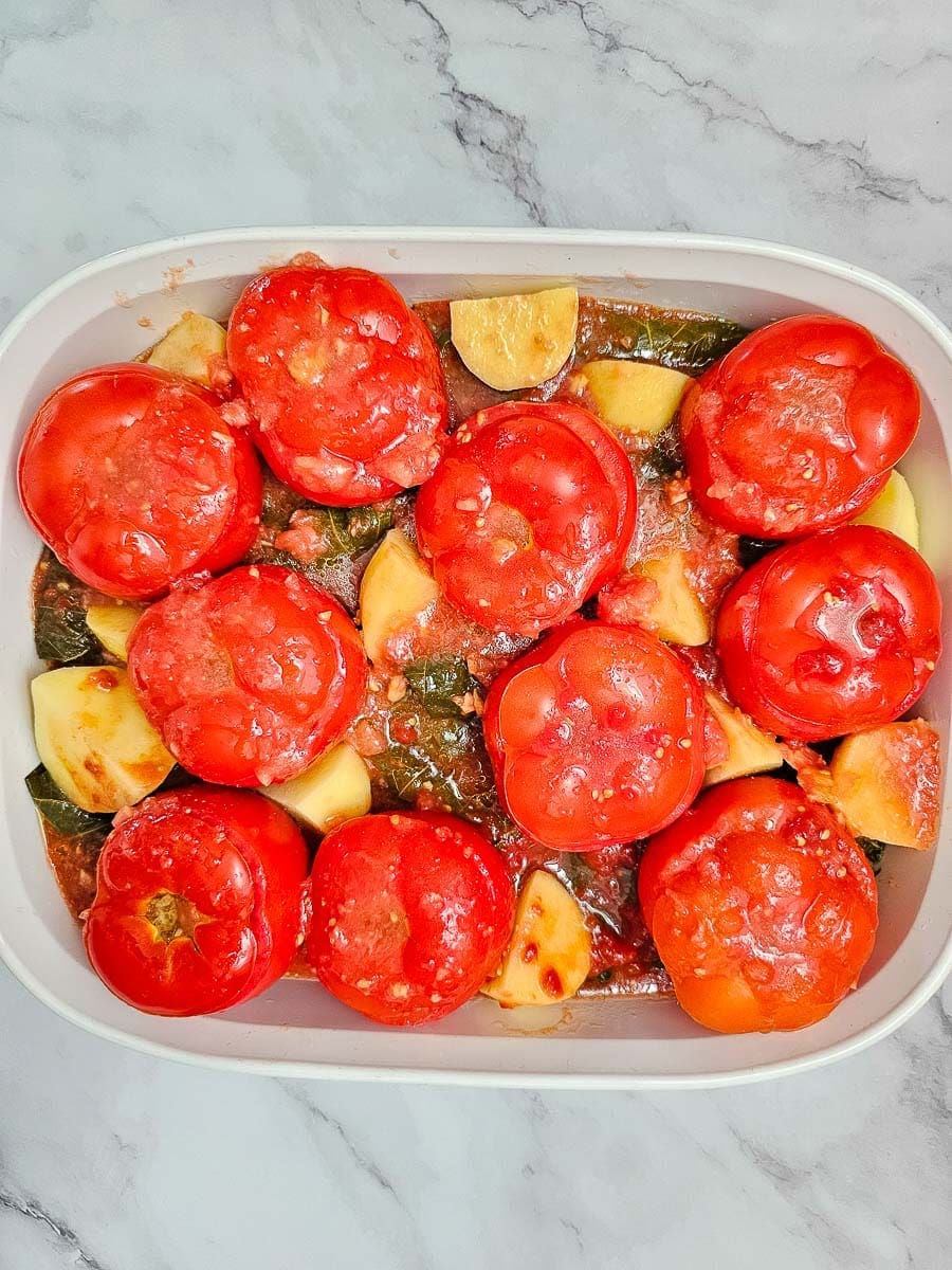 Yemista, stuffed tomatoes with rice, in baking dish with potatoes and vine leaves and tomato olive sauce.