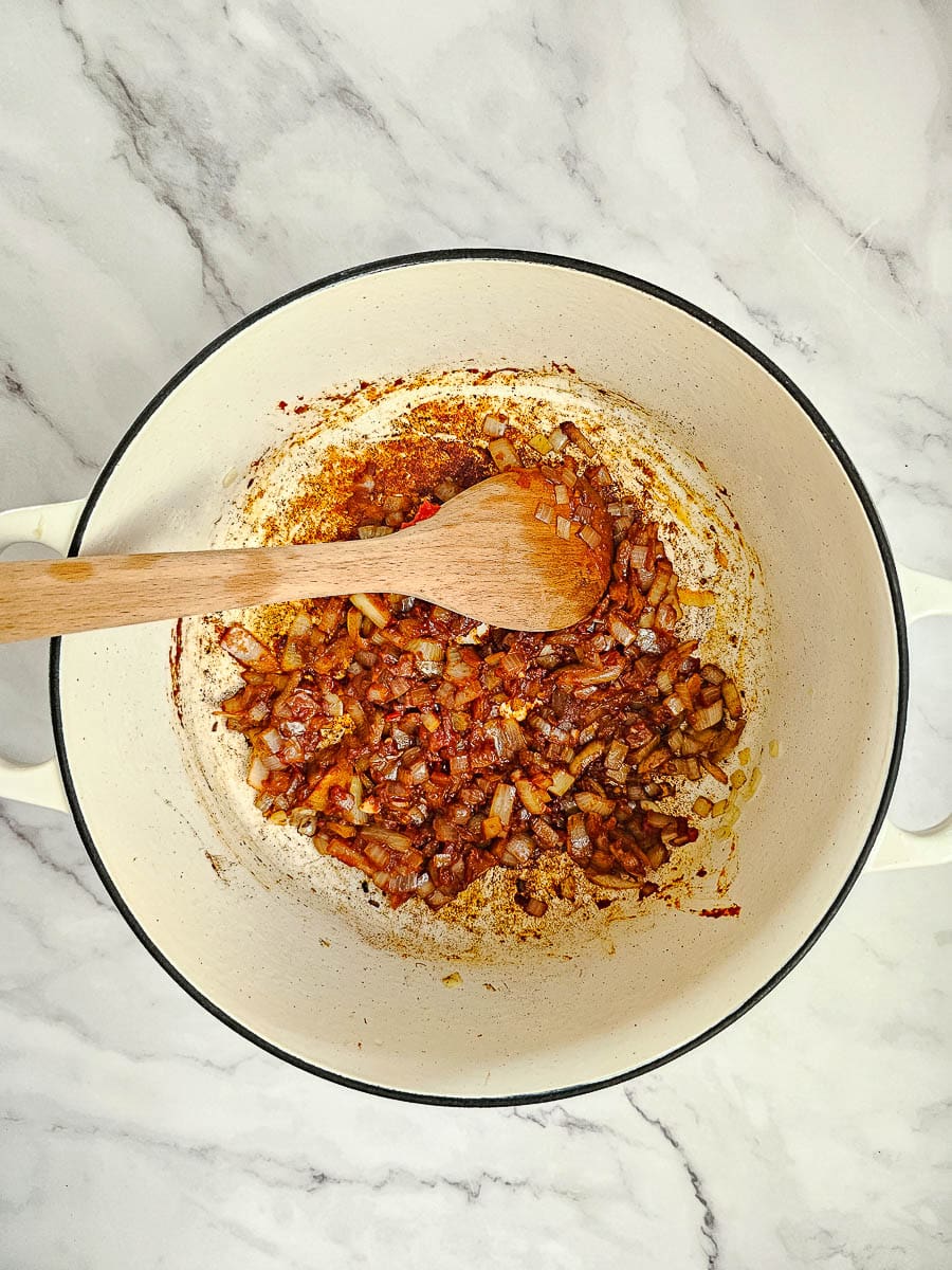 sauteing onions and garlic in pot with a wooden spoon and adding tomato paste