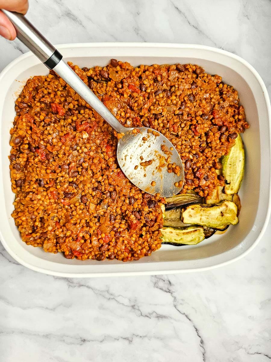 spreading lentil sauce over vegetable layer for vegan moussaka