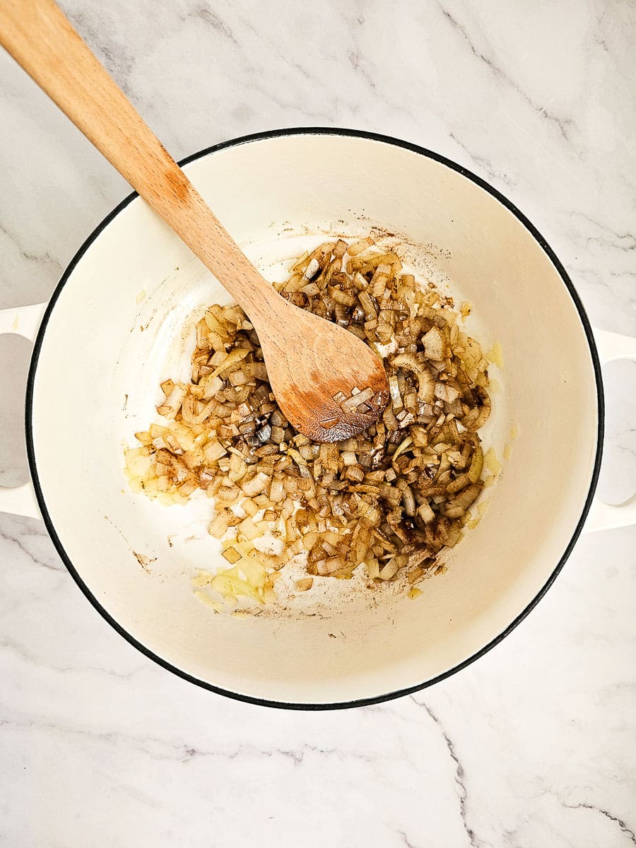 sauteing onions and garlic in pot with a wooden spoon and adding spices