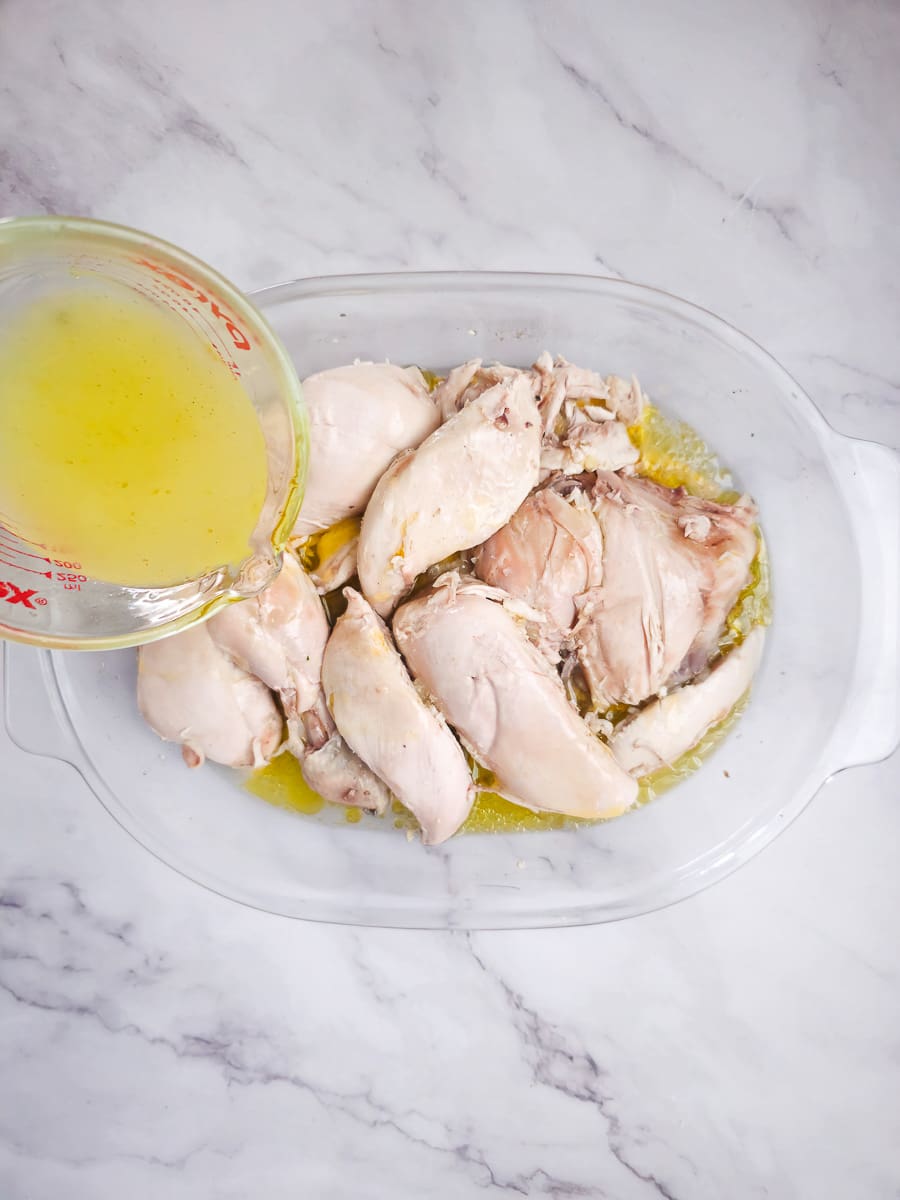 pouting lemon and olive oil mixture over boiled chicken in a baking dish