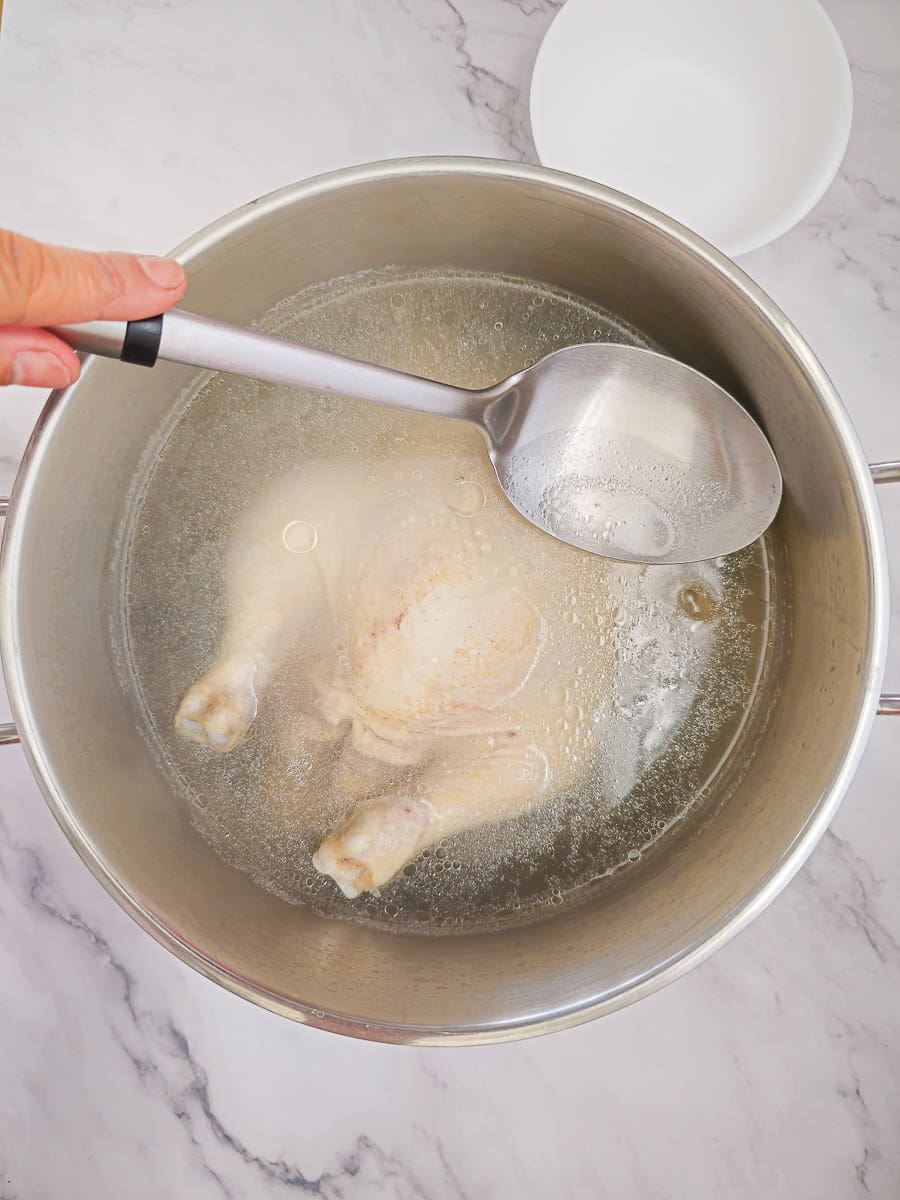 skimming foam with a spoon from whole chicken in a saucepan