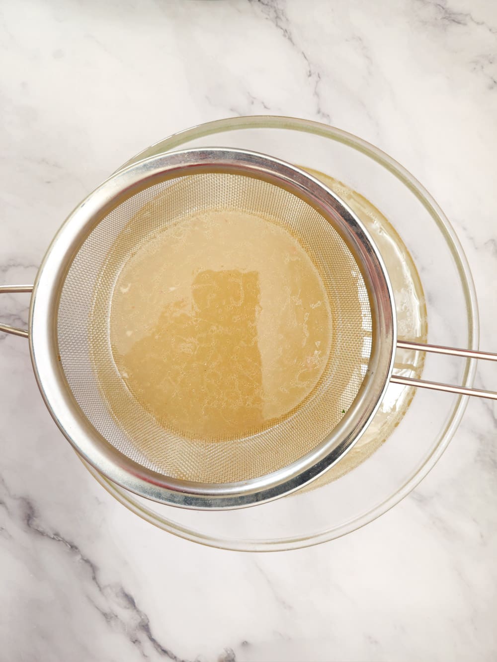 strain chicken broth in a large bowl with a strainer