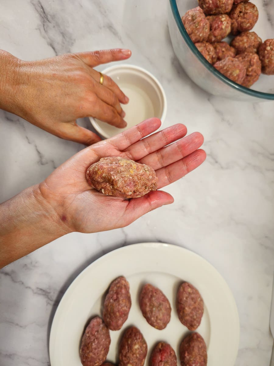 Shaping Soutzoukakia - Greek meatballs in hand and adding dipping fingers in water