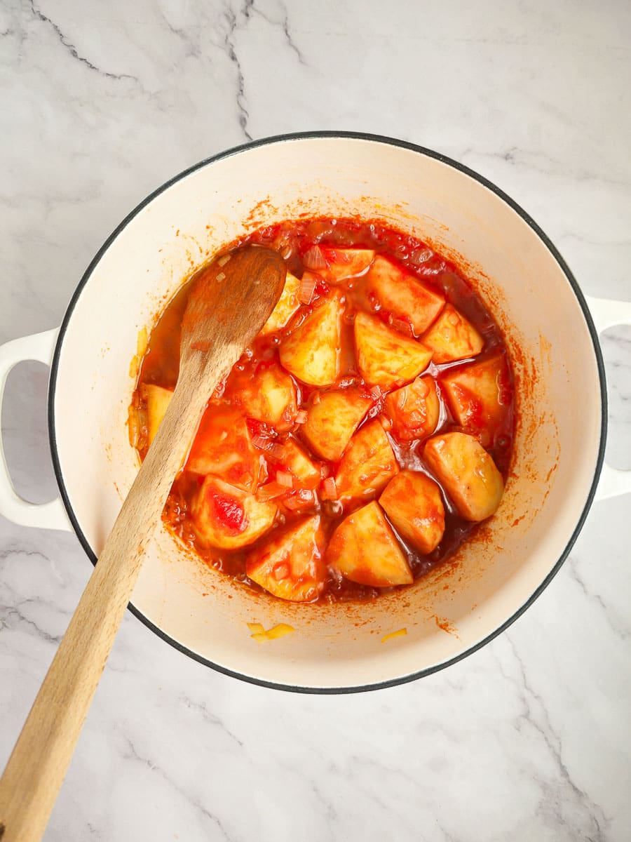 adding tomatoes to pot with wooden spoon