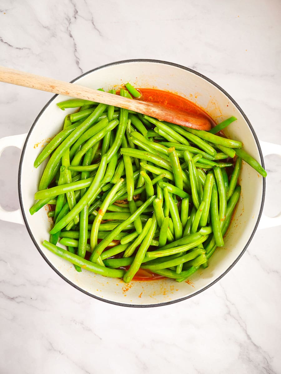 Fasolakia -Green Beans with potatoes in a pot and wooden spoon