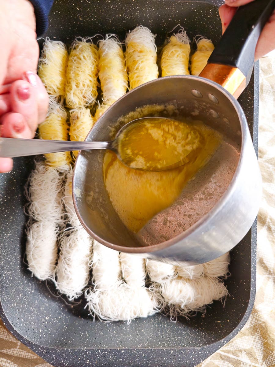 spooning melted butter over Rolling Kataifi - Greek String Pastry Nut Rolls before baking