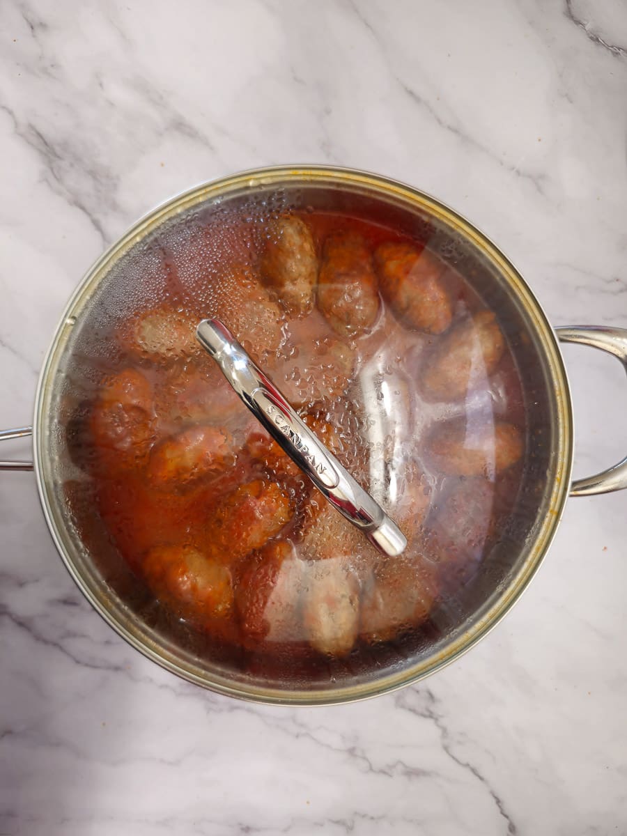 Soutzoukakia - Greek meatballs in tomato sauce in a pan simmering with lid on