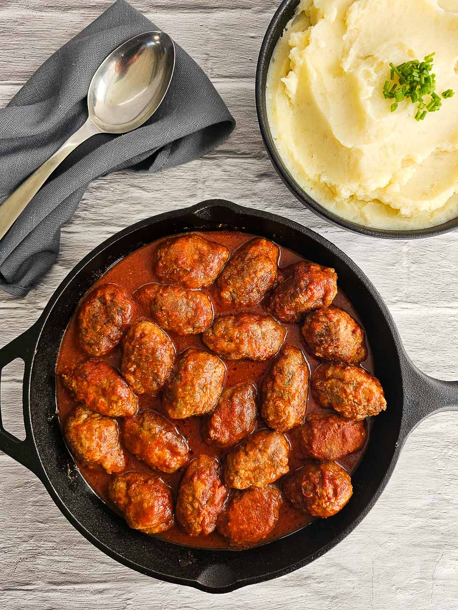 Soutzoukakia - Greek meatballs in tomato sauce in a pan with mashed potato on the side in a bowl