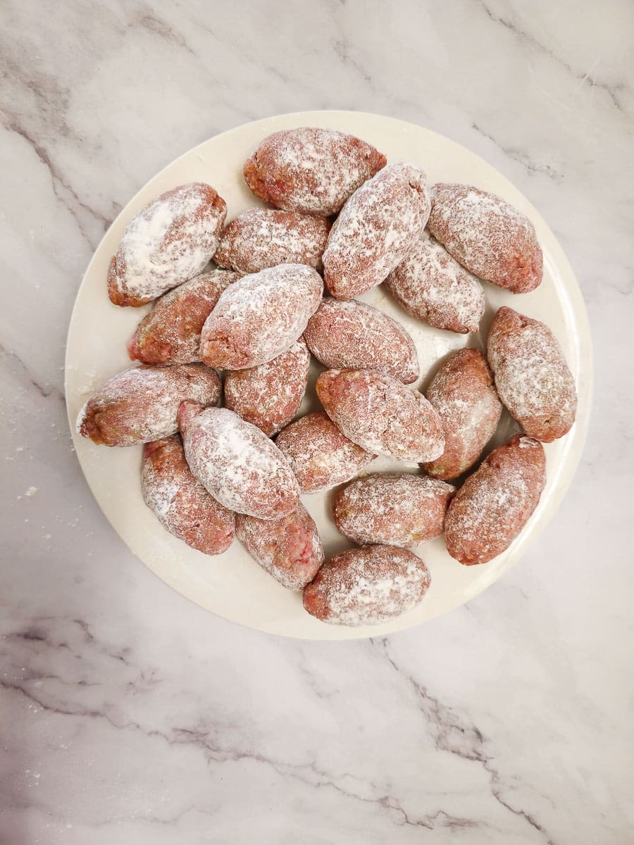 Soutzoukakia - Greek meatballs on a plate coated in flour before frying 