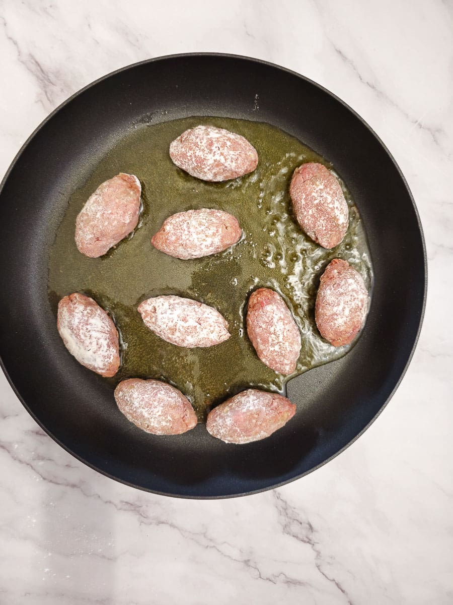 Frying Soutzoukakia - Greek meatballs in tomato sauce in a pan