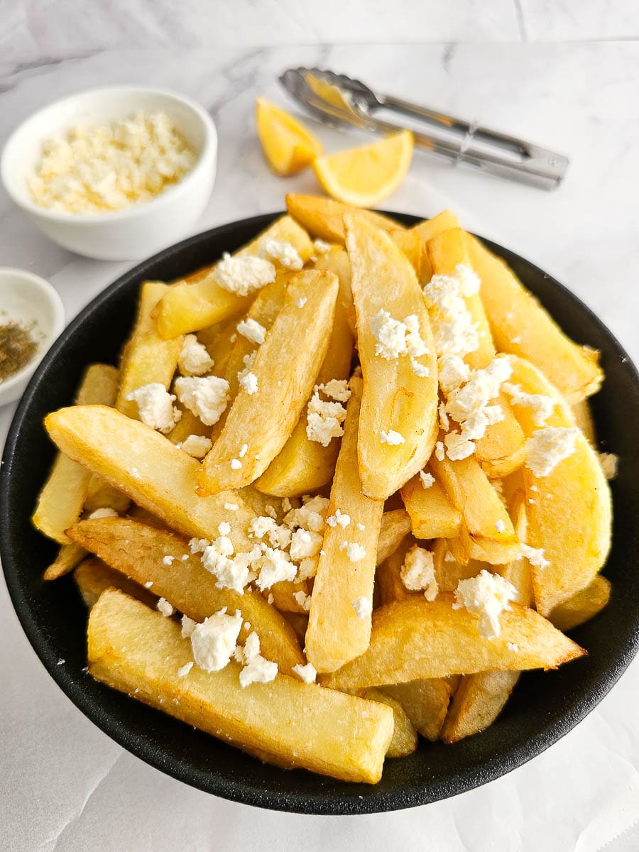 Greek Olive Oil Fries - Patates Tiganites, in a bowl with crumbled feta