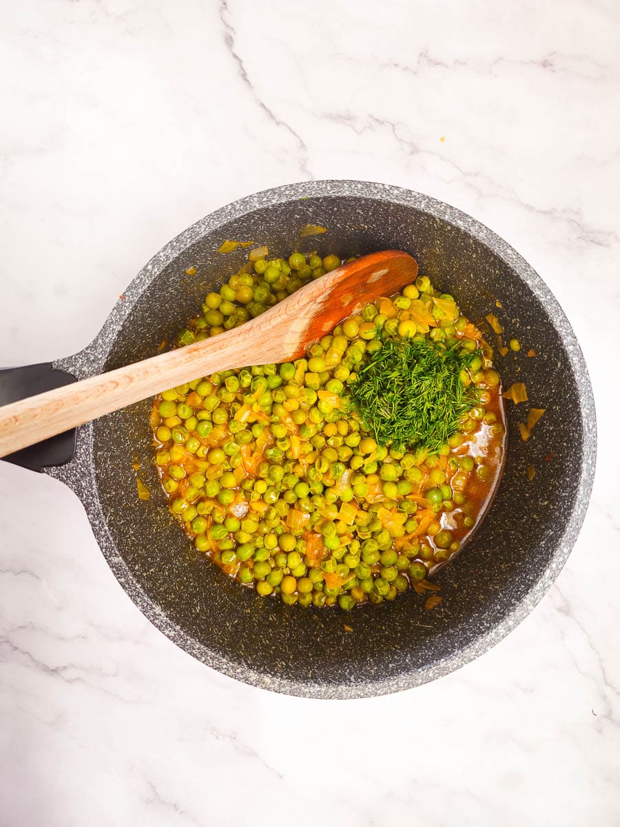 Greek Peas in Tomato Sauce (Arakas Latheros) in a pot with a wooden spoon and adding dill. 