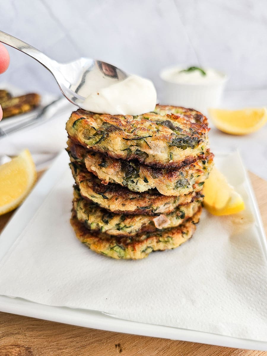 Greek Zucchini Fritters - Kolokithokeftedes stacked on board with a spoon of tzatziki