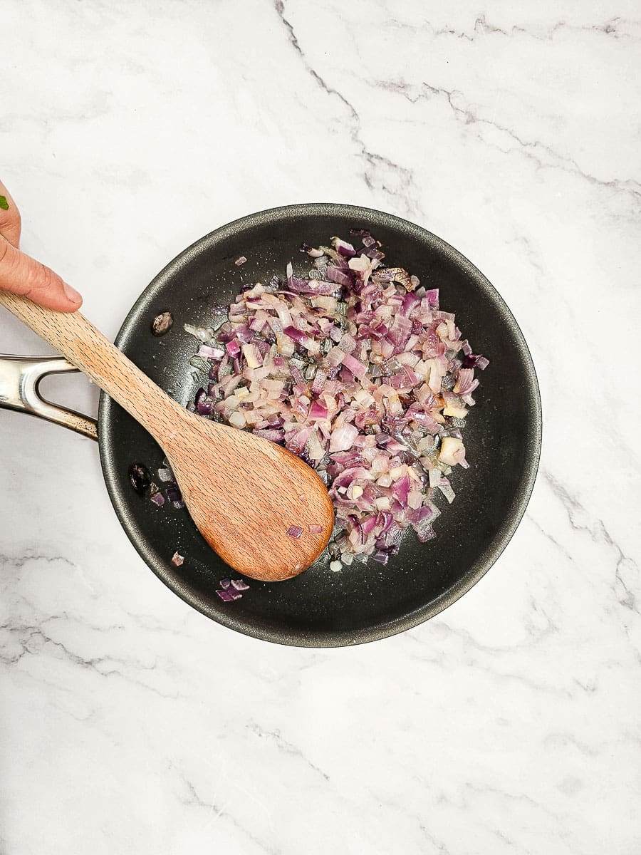 frying diced red onion in pan with wooden spoon