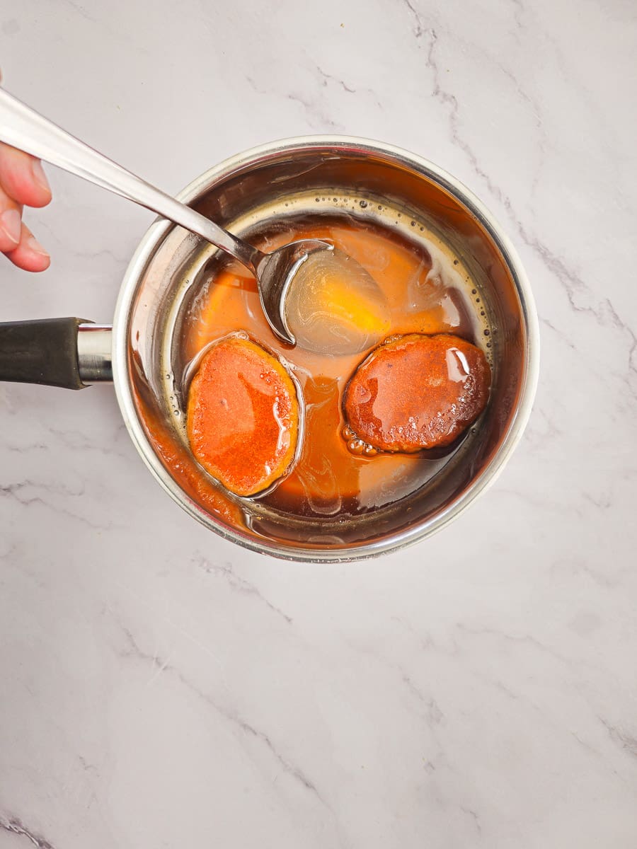 soaking melomakarona in honey syrup in saucepan