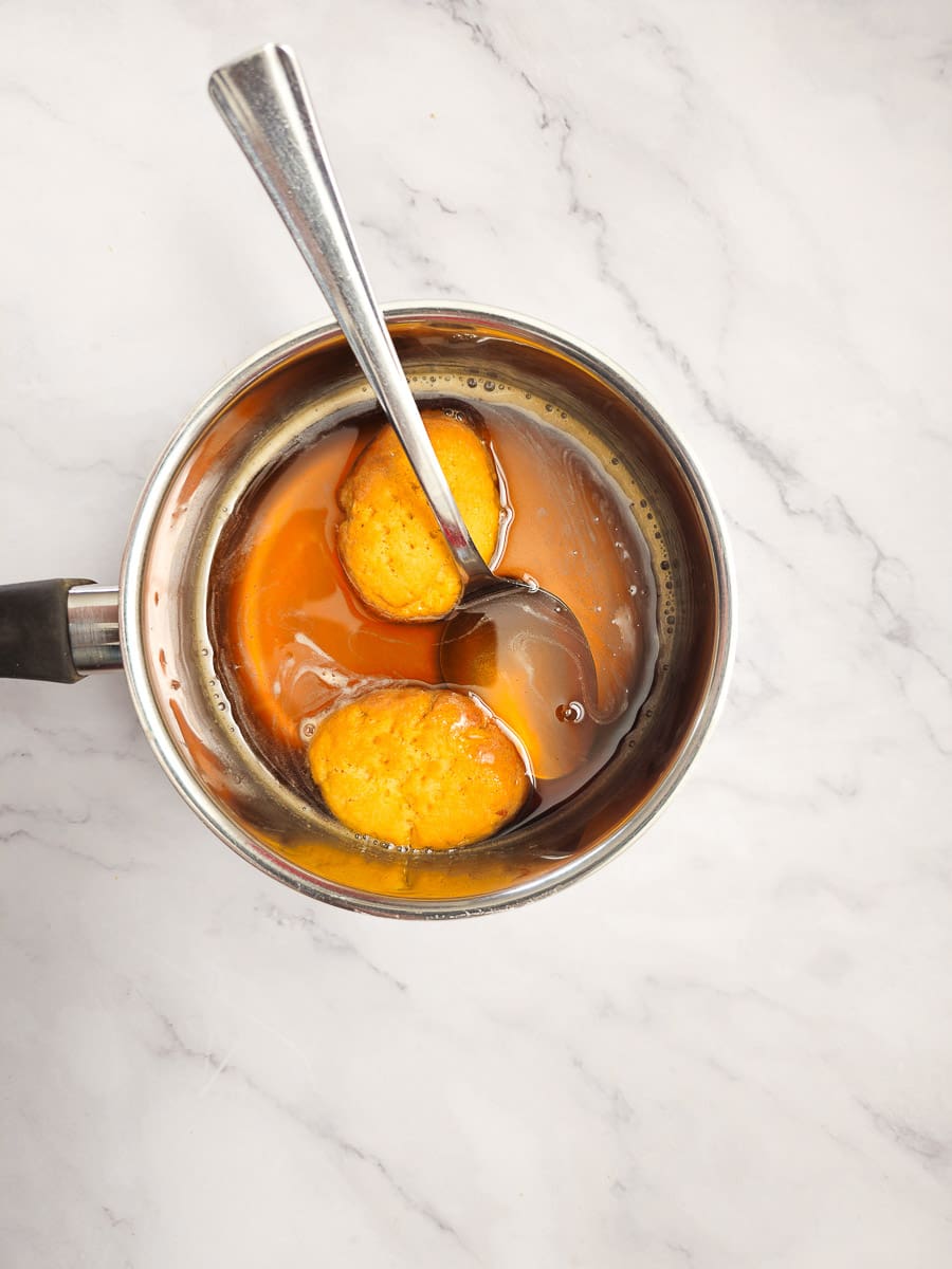 soaking melomakarona in honey syrup in saucepan