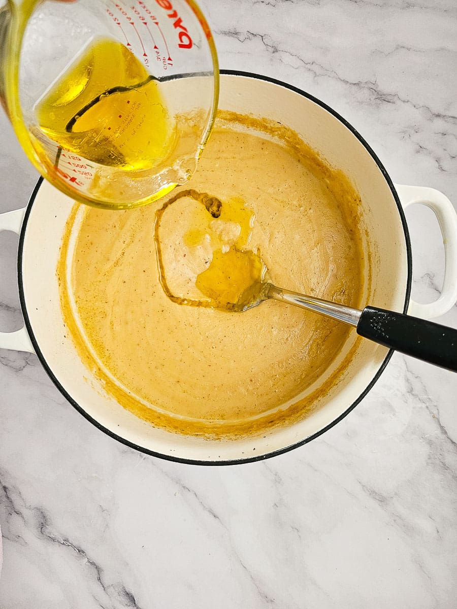 adding olive oil to fava- yellow split pea puree in a pot