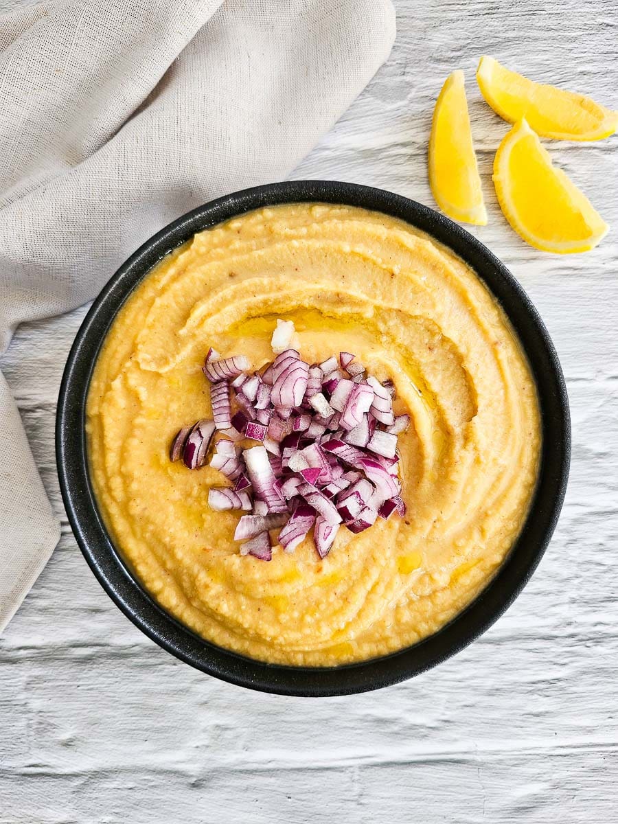 Fava- yellow split pea puree in a bowl with diced red onion