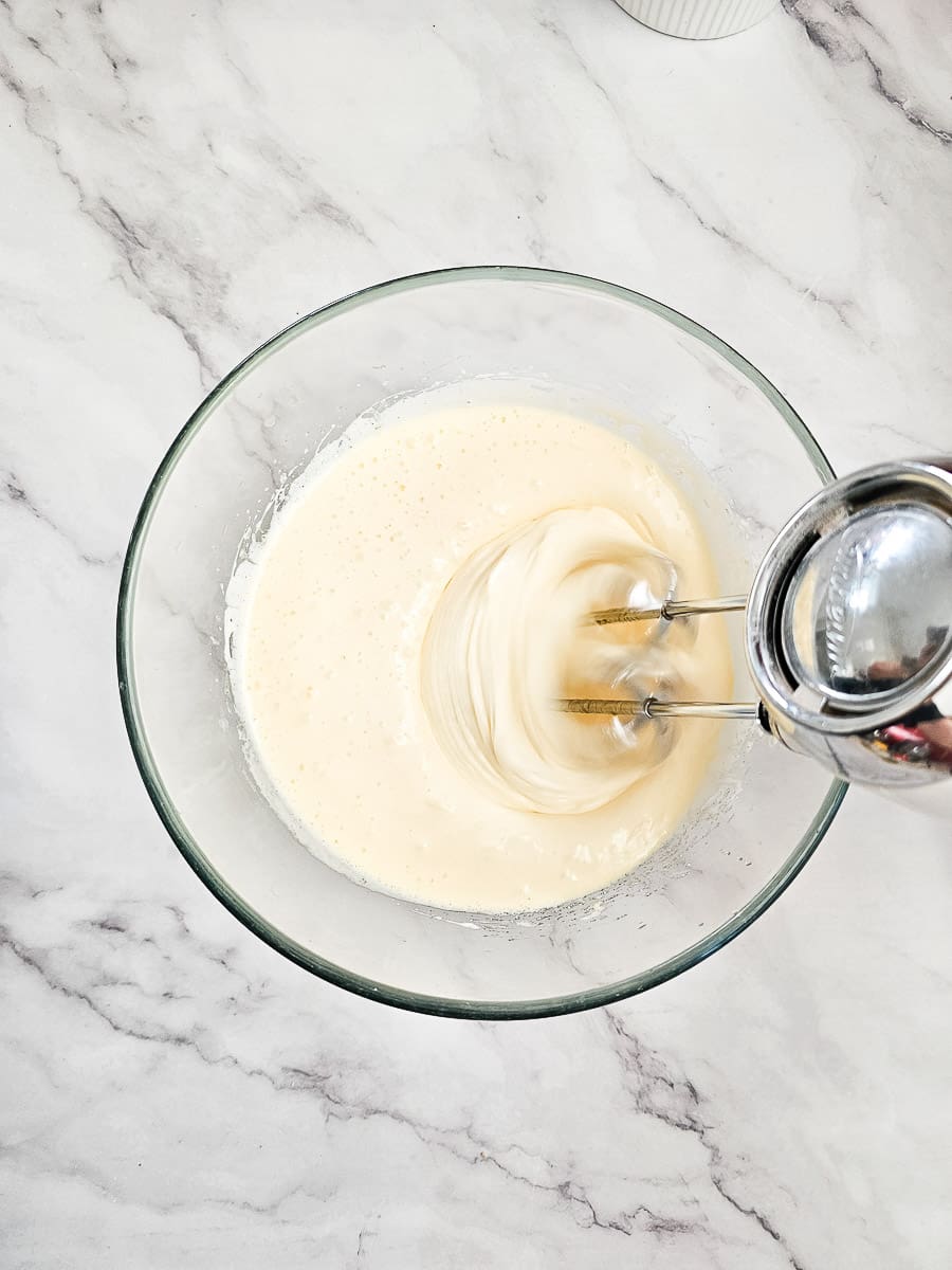 beating eggs and sugar in a bowl with hand beater